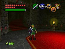 The child version of the game's protagonist, Link, stands in Hyrule field wearing his distinctive green tunic and pointed cap. In each corner of the screen are icons that display information to the player. In the upper left-hand corner, there are hearts, which represent Link's health, in the lower left-hand corner is a counter that displays the number of Rupees (the in-game currency) possessed by the player. There is a mini-map in the lower right-hand corner, and five icons in the upper right-hand corner, one green, one red, and three yellow, which represent the actions available to the player on the corresponding buttons of the N64 controller.