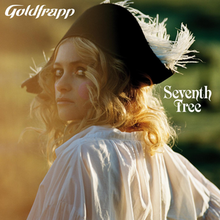 Alison Goldfrapp in a black pirate hat and white dress, looking over her shoulder into the camera