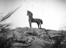 In the distance, a model wooden horse sits atop a hill.
