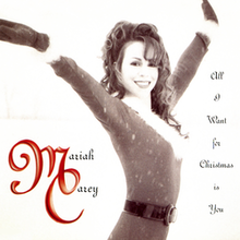Carey wearing a Santa suit, while posing in an upright position. She has long brown curly hair, and is smiling. The background imagery is a pastel version of yellow, almost a beige color, with red letters that spell out the song's title.