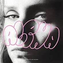 A closeup, black-and-white photograph of the artist's face, staring directly into the camera with a serious look, with the word "Alpha" written in pink bubble letters on top.