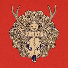 A black and white drawing of a deer's skull with large antlers on a red background, in the middle of a round pattern with many patterned circles. Above the skull is a smiling face, with two hands holding onto its antlers. In the middle of the pattern are the letters "YANKEE" written in white.