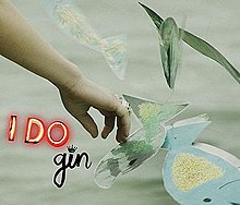 Woman's hand reaching for paper cut-outs of fish, with red neon "I DO" and black "gin" to the bottom left.