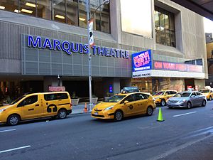 A large sign with lighted letters reading "Marquis Theatre" next to a marquee advertising the theatre's current show