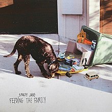 A dog searches the lid a fallen garbage bin filled with cardboard boxes of superimposed images of city buildings. Hand-written text at the bottom states the band name and EP title.