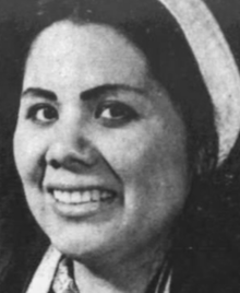 A smiling young Native American woman, dark hair in a white headband