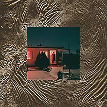 A photo of a man standing inside the doorway to a bungalow with a thick border of crumpled golden foil around it