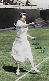 A brown-haired woman is wearing all white clothing, and is hitting a tennis shot.