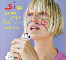 Sia stands against a light blue background, holding some markers in front of her face. There are drawings on her face. To the left of her, the name "Sia" and the title "Some People Have Real Problems" is stylized in a colorful, handwritten font.