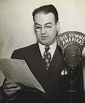 Black and white photograph of a male wearing glasses and standing next to a microphone