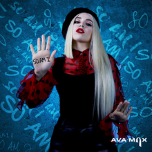 Max is seen wearing a black beret and a red outfit, as she displays the palms of her hands. The words 'So Am I' are written on her right hand, with the blue background displaying the repeating text on a diagonal slope.
