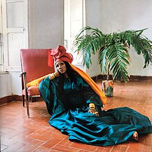 A photo of Koné sitting on the floor, wearing a long, blue-green gown.