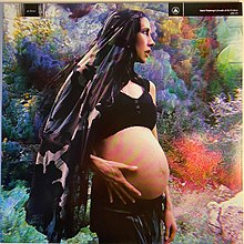 A photo of Hart late in her pregnancy with Yupanqui, stood in front of a large multicolored bush.
