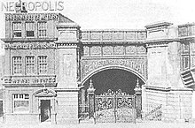 Three-story office building next to a railway arch, with an ornate gate in front of it.