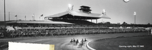 A black and white photograph depicting a race at Rosecroft. Six horses are making a turn, and 6,000 people are watching.