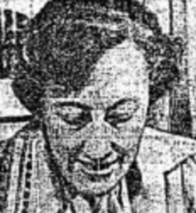 An older white woman, gaze cast downward