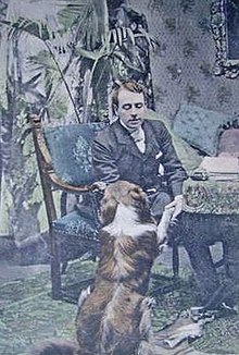 youngish, clean shaven white man in late Victorian or Edwardian day wear, seated looking at playful dog at his side