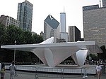 A white outdoor sculpture is fenced off from the public with a backdrop of tall buildings