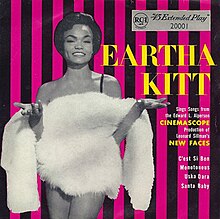 Eartha Kitt wearing a feather boa in front on a pink and black-striped background.