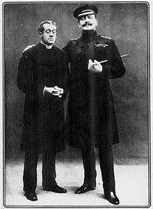 small clergyman standing next to upright military man