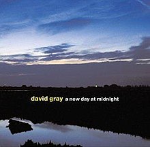 A photograph of a sunrise over a body of water with the artist and album title overlaid
