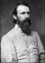 Photo shows a black-bearded man in a gray military uniform.
