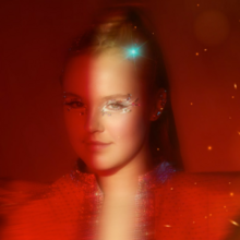 A fuzzy, red-toned image is illuminated by a vertical column of light cast on JoJo Siwa's bejeweled left eye.