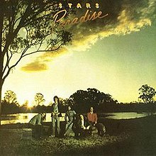 An outdoor rural scene at twilight shows a cloudy sky overhead and a large tree at left. In the background are more trees with a lake or river in middle distance. In the foreground are five men. The first at left is sitting with his right side showing while leaning forward and facing slightly toward the viewer. His hair is dark and over shoulder length, he has a dark moustache and he wears a denim jacket, dark pants and dark shoes. The second man is the only one standing, he faces the viewer and has his thumbs tucked into the top of his denim jeans. His hair is also over shoulder length and is swept over his left, he wears a tropical-themed shirt, dark jacket and runners. The third man is sitting facing forward, his hair is shoulder length and he has a beard. He wears a denim shirt and denim jeans with brown shoes. The fourth man is sitting facing forward and his hair is just over his shoulders. He wears a dark jacket and dark pants. The fifth man is wearing a red shirt and dark pants with brown boots. His hair is shoulder length and he has a moustache. At the top is the group's name and just below is the album title.