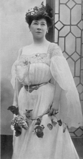 youngish white woman, with dark hair in Edwardian day clothes, holding flowers
