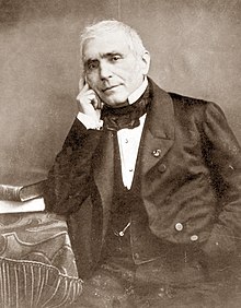 white man in late middle age, seated. He is clean shaven, and has white hair