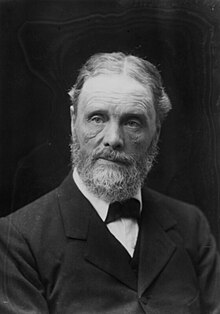 An ageing man in a formal suit with a beard