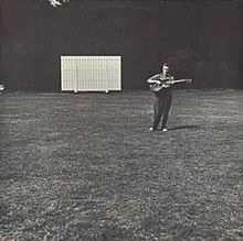 The album cover is a black-and-white photograph of a cricket field with a sight screen in the distance, off-center to the left. Off-center to the right and in the distance Fred Frith is standing playing a guitar. There is no text on the cover.