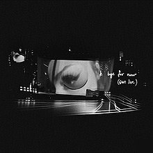 A black-and-white photo of a Sweetener World Tour concert, prominently displaying Ariana Grande's left eye through a large screen. On the right side of the image lies handwritten text that reads "k bye for now"; below it is a parenthetical that reads "(swt live)".