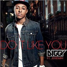 A man sporting an open jean jacket with rolled up sleeves, a white t-shirt and a hat stands behind a Brownstone. The song title and featured artist's name are colored in red while the artist's logo is between them.