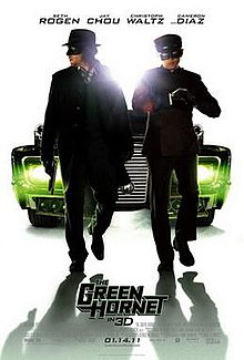 Two suited masked men, behind them is a large car them with green headlights.