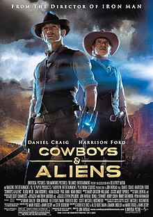 In the desert, a cowboy wearing a glowing bracelet stands next to an older cowboy, as a similar glow shines behind them.