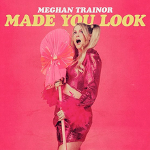 一位身穿粉红裙子并拿着道具的金发女子，上方则印着“Meghan Trainor Made You Look”的字样