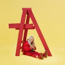 Eilish is seen sitting below a red ladder, holding jewelry that is around her neck.